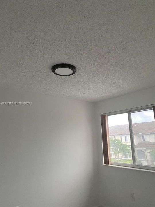 Interior room featuring white-painted walls, a textured ceiling, and a circular flush-mount ceiling light with a dark frame