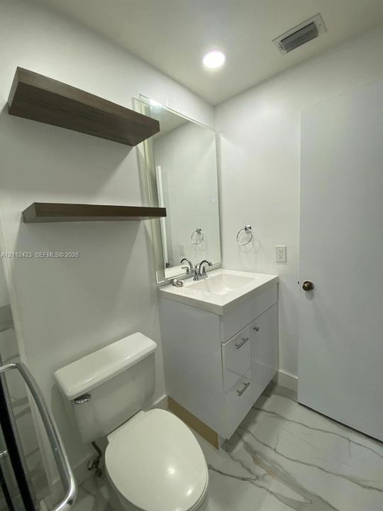 Modern vanity featuring a white cabinet, integrated sink, and chrome faucet, complemented by wall-mounted wood-finish floating shelves, a large wall mirror, and stone-finish tile flooring