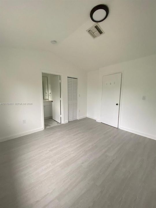 Neutral-toned wood-finish flooring, vaulted ceilings, and louvered closet doors
