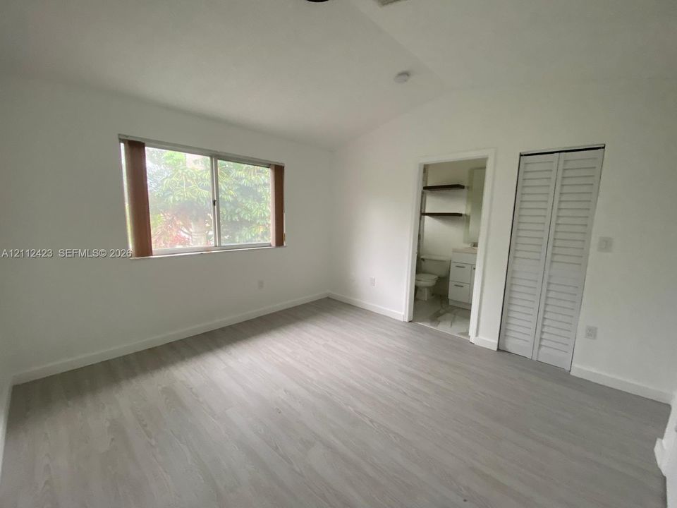 Interior space featuring wood-finish flooring, a sliding window with horizontal blinds, and a built-in closet with louvered bifold doors