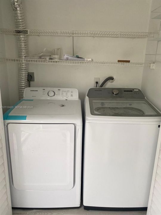 Laundry closet featuring side-by-side washer and dryer units with dual-level white wire shelving