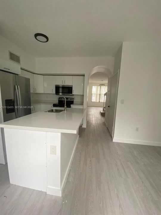 Kitchen featuring a stone-surface island, stainless steel refrigerator, flat-panel white cabinetry, wood-finish flooring, and an arched entry