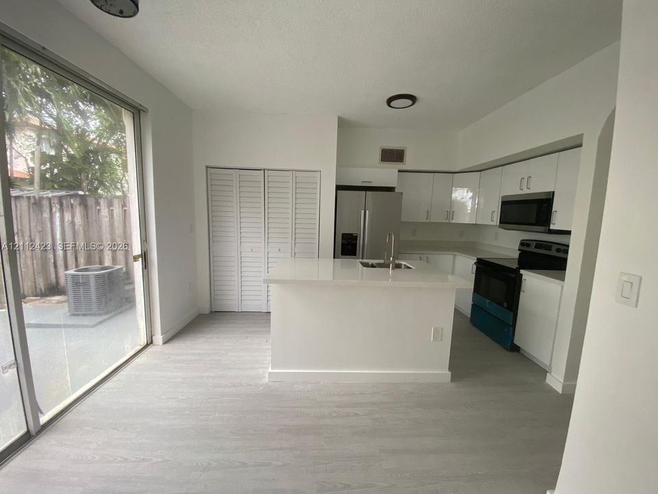 Kitchen featuring white cabinetry, a center island with a stone-finish countertop, stainless steel appliances, sliding glass doors, and wood-finish flooring