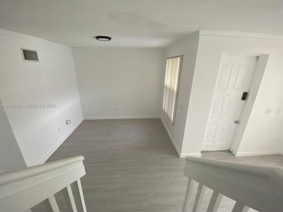Interior space featuring wood-finish flooring, a six-panel door, crown molding, and a minimalist flush-mount ceiling light fixture