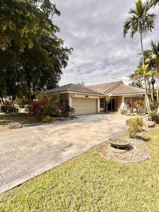 Single-story residence featuring a tile roof, an attached two-car garage, an expansive concrete driveway, and established palm and tropical landscaping