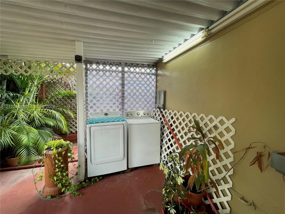 Covered outdoor laundry area featuring white lattice wall panels, corrugated metal ceiling, and concrete flooring