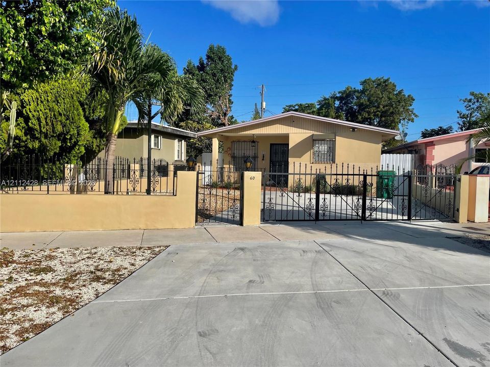 Single-story residence featuring a concrete driveway, gated perimeter wall, ornate metal fencing, and a covered entryway