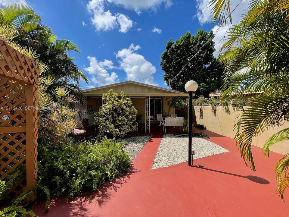 Enclosed courtyard featuring painted concrete flooring, stone-accented ground cover, decorative wood lattice screening, and mature tropical landscaping