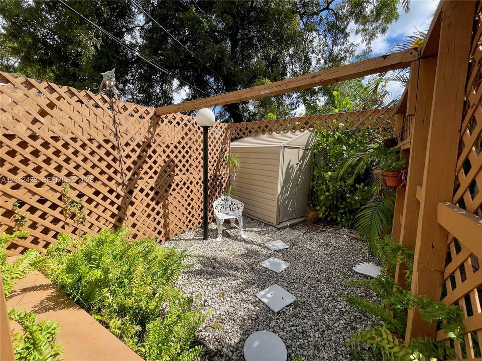 Enclosed outdoor space featuring wood lattice perimeter fencing, gravel ground cover, a built-in storage shed, and integrated post lighting