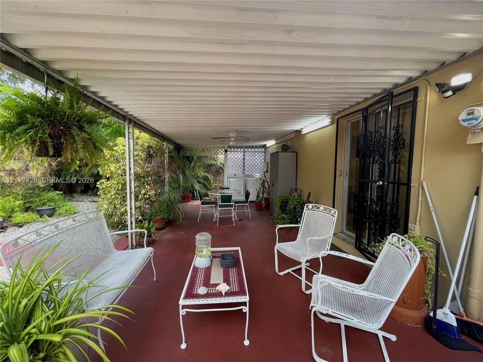 Covered outdoor patio featuring a solid metal roof, painted concrete flooring, wall-mounted exterior lighting, and an iron security screen door
