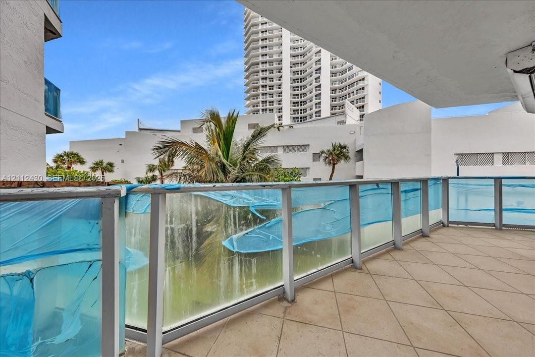 Covered balcony featuring tile flooring and a glass railing with metal framing