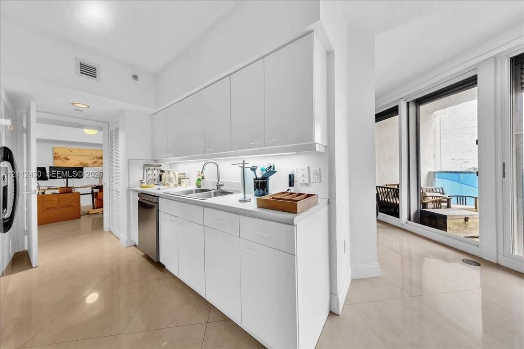 Kitchen featuring flat-panel high-gloss cabinetry, stone-finish countertops, stainless steel undermount sink, integrated stainless steel dishwasher, and polished tile flooring
