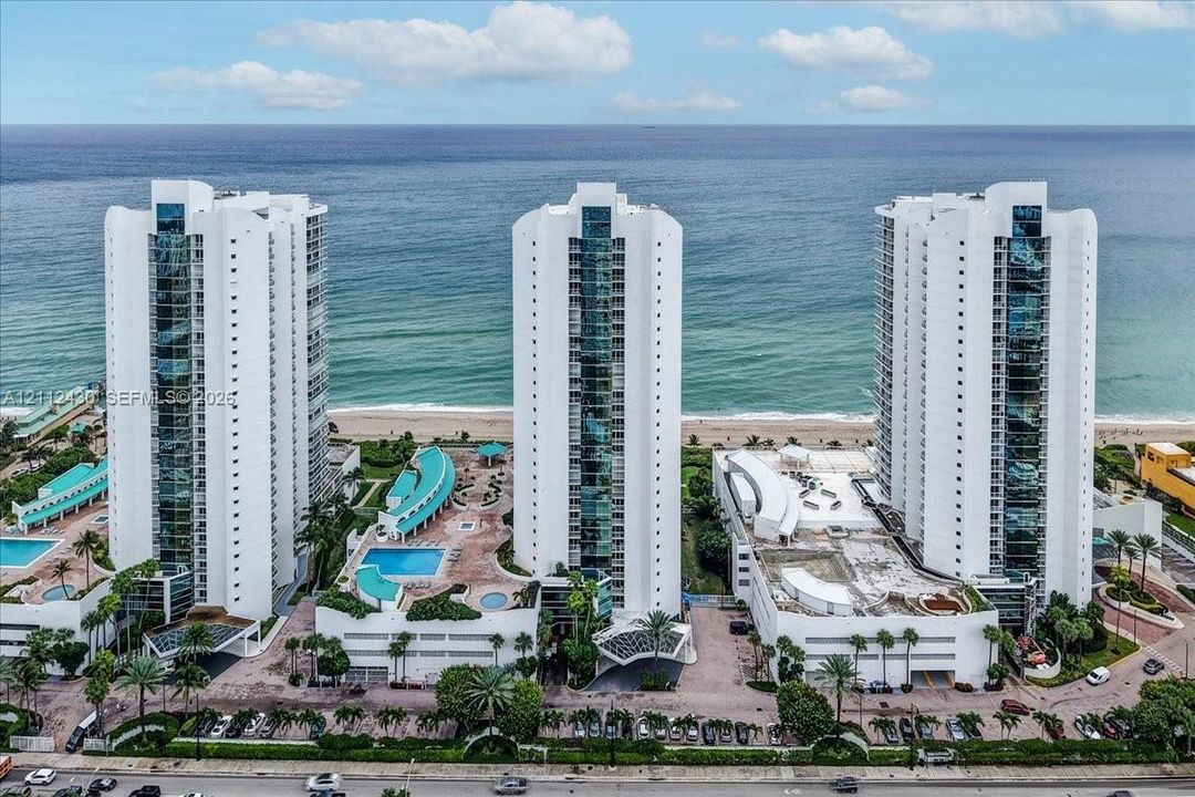 High-rise residential complex featuring oceanfront positioning, multiple swimming pools, tiered sun decks, and mature tropical landscaping