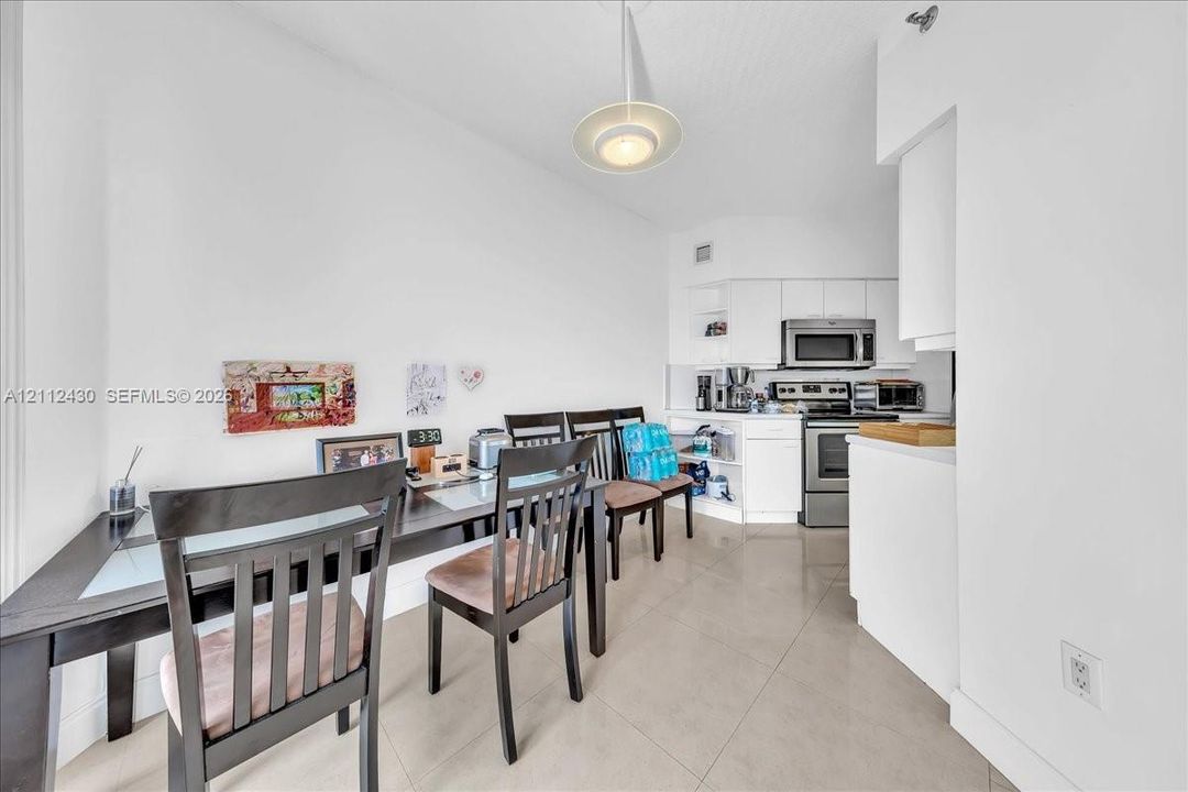 Kitchen area featuring white cabinetry, stainless steel appliances, large-format tile flooring, and a contemporary pendant light fixture