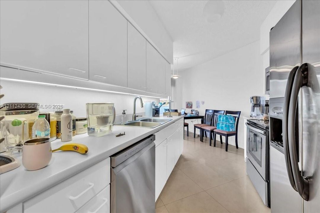 Kitchen featuring flat-panel white cabinetry, solid-surface countertops, stainless steel appliances, under-cabinet lighting, and large-format tile flooring