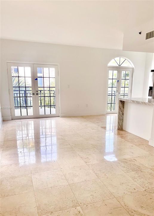 Polished stone flooring throughout, dual sets of glass-paned French doors, arched transom window detail, and a breakfast bar with stone-surround base