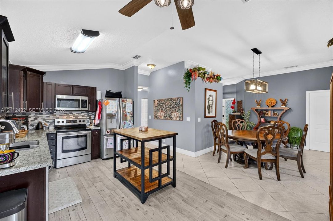 Kitchen featuring dark wood cabinetry, stainless appliances, multi-tonal tile backsplash, and granite-finish counters, accented by a pendant light fixture and wood-looktile flooring