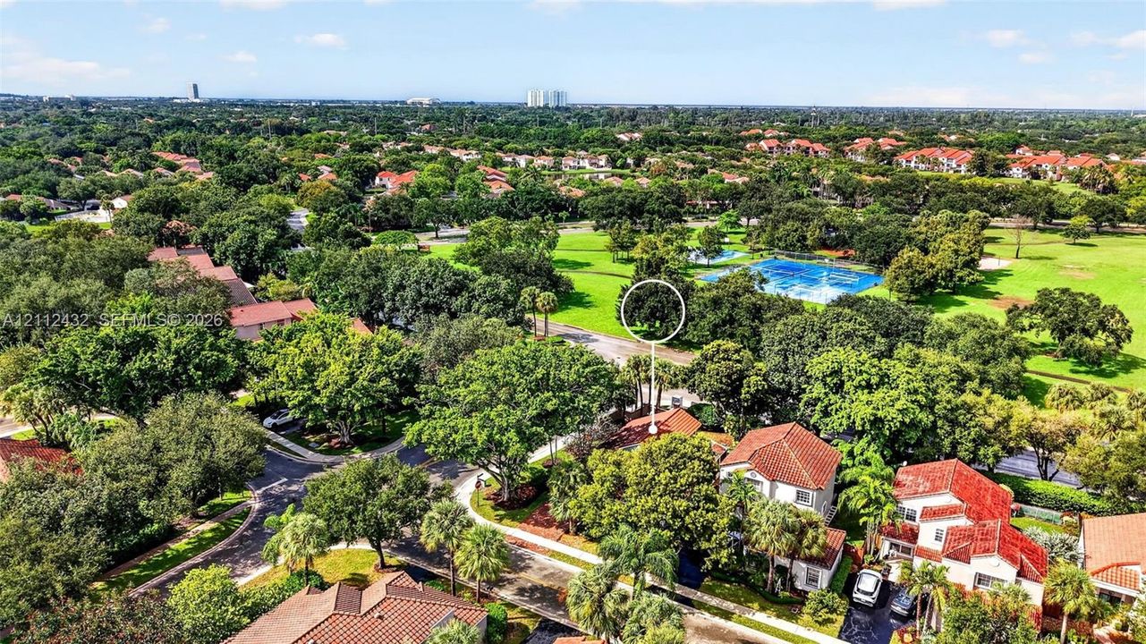 Aerial perspective showcasing a residential setting with mature tree canopy, tile roof architecture, and proximity to expansive green space