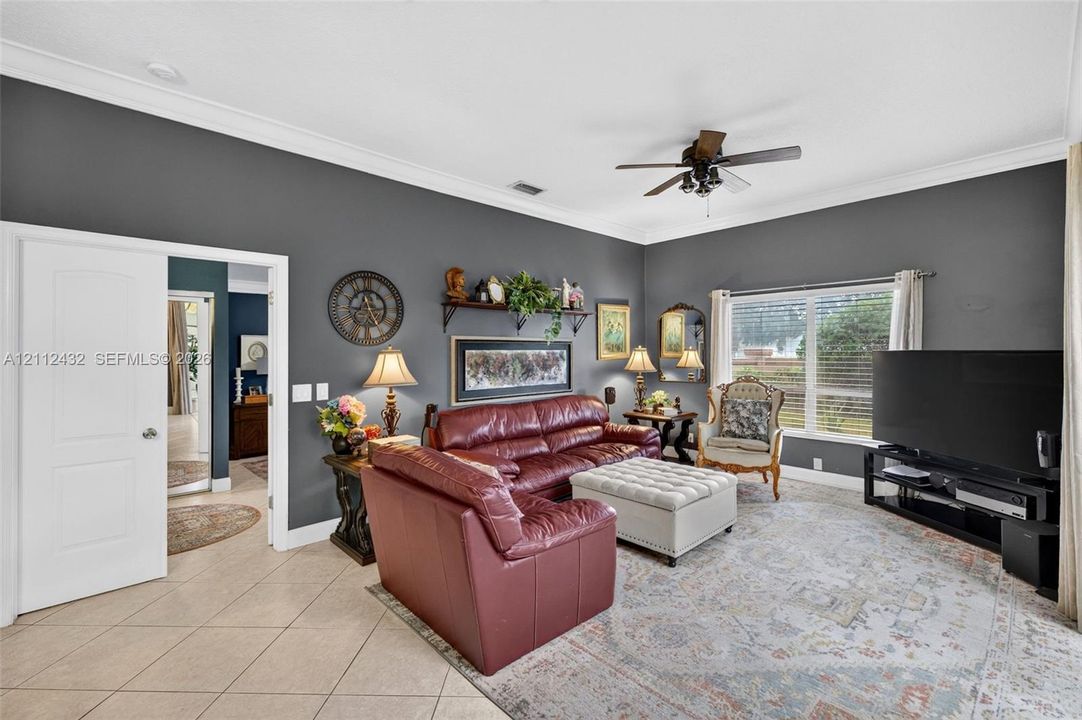 Living area featuring high ceilings with crown molding, neutral tile flooring, and a ceiling fan