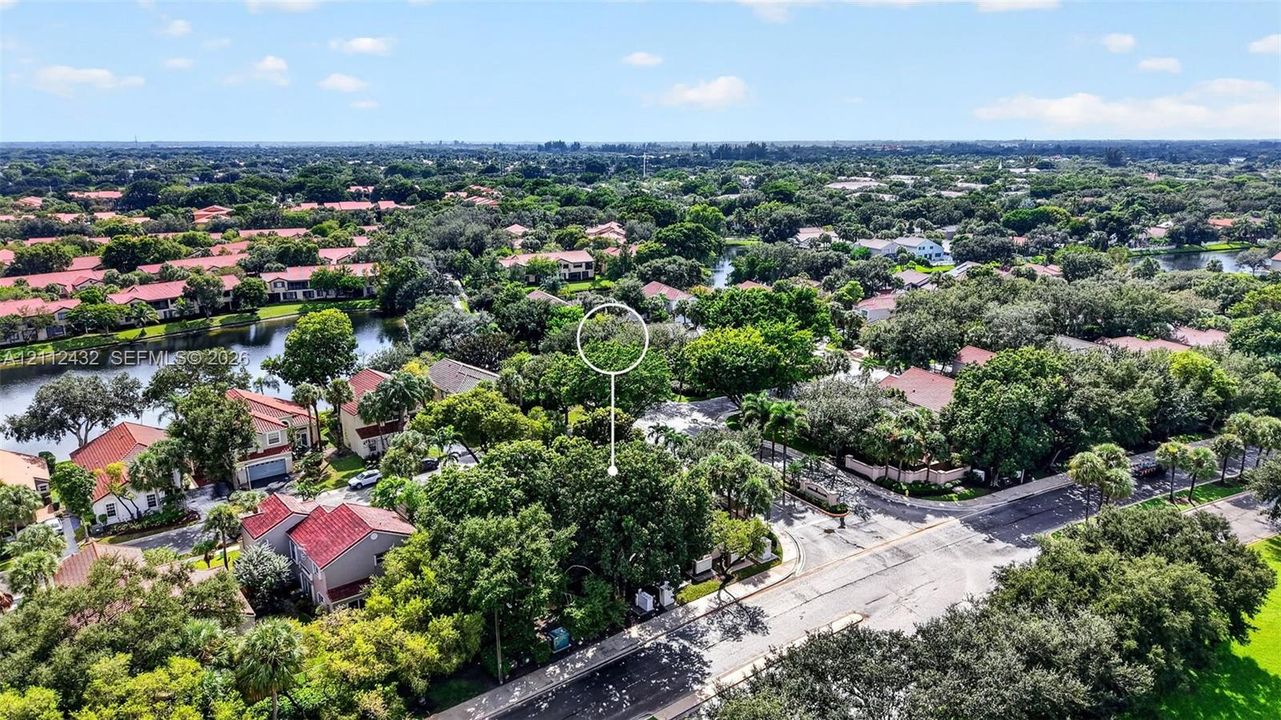 Aerial perspective of a residential community featuring mature trees, a winding water feature, paved roadways, and dense canopy cover