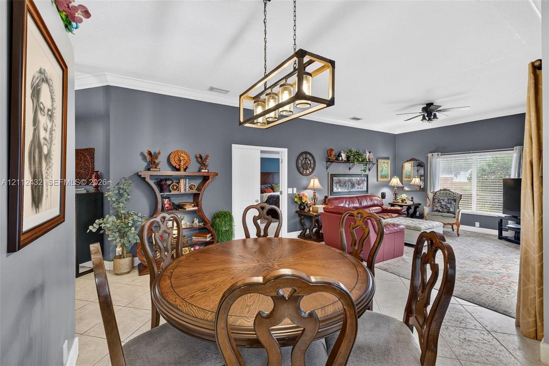 Open floor plan featuring tile flooring, crown molding, and a geometric-frame pendant light fixture