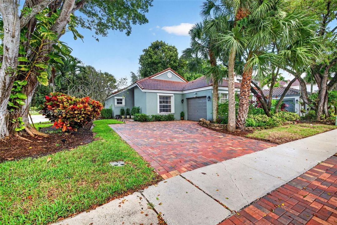 Single-story home featuring a 2015 tile roof, 2025 paver driveway, attached garage, and beautiful established landscaping with mature palm trees