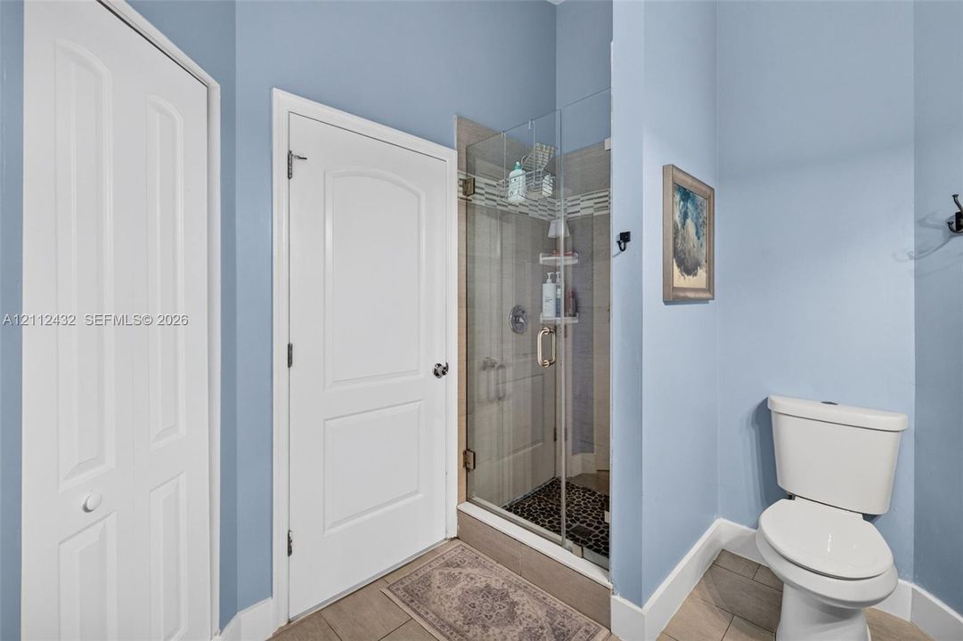 Bathroom featuring a frameless glass shower enclosure, tiled wall surround, stone-tiled shower floor