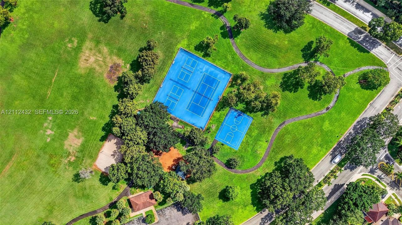 Expansive green space featuring tennis courts, a basketball court, paved pathways, and mature trees