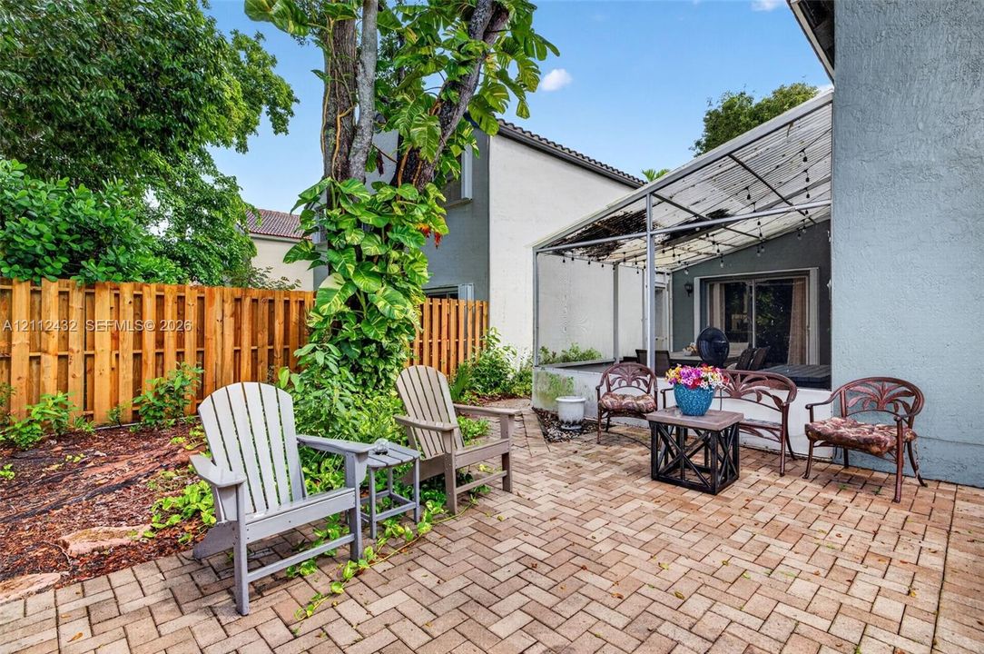 Paver patio featuring a metal-framed covered lanai and mature landscaping