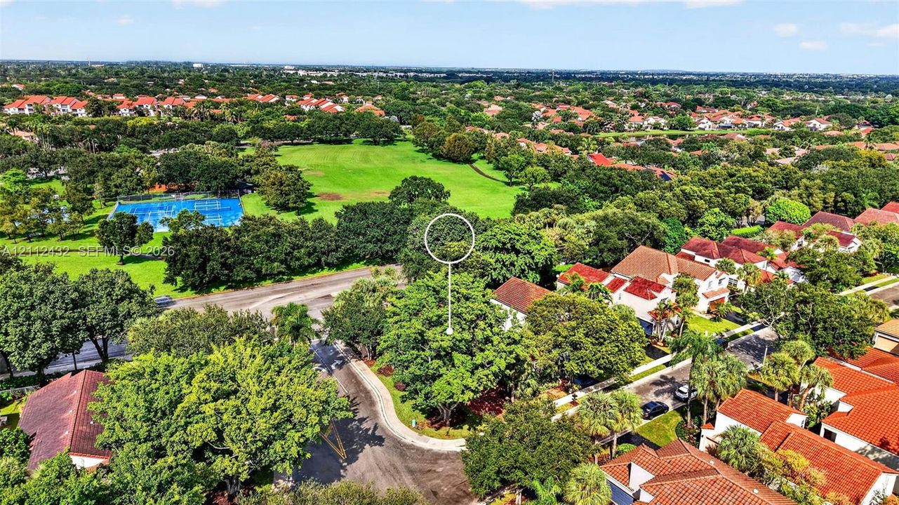 Aerial perspective of residential property featuring a cul-de-sac location, mature tree canopy, and proximity to expansive green space and recreational courts