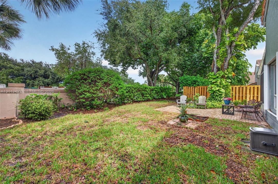 Private backyard featuring a paved stone patio, mature canopy trees, sculpted shrubbery