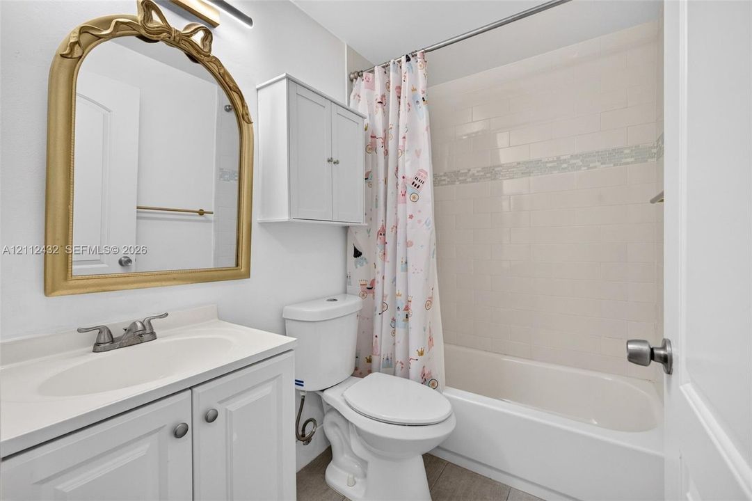 Bathroom featuring a white vanity cabinet with an integrated sink, a wall-mounted storage cabinet, a bathtub with tile surround, and an arched wall mirror