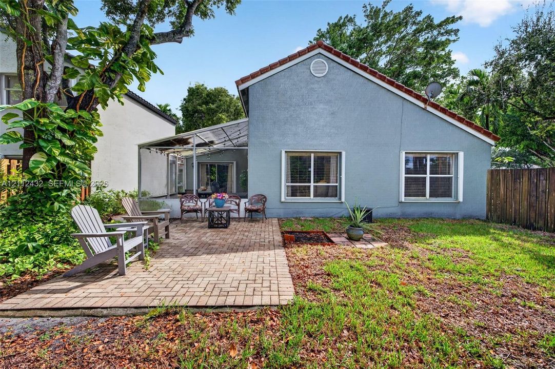 Rear exterior featuring a brick paver patio, screened-in enclosure, stucco siding, and a gabled roof