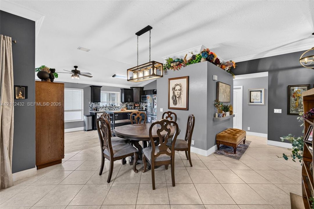 Open-concept interior featuring light-toned tile flooring, a central decorative wall divider, a rectangular multi-light pendant fixture, and crown molding