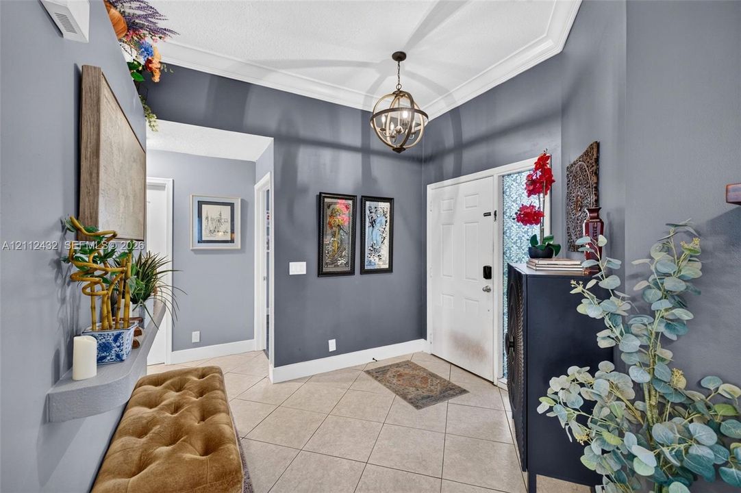 Foyer featuring large-format ceramic tile flooring, crown molding, a decorative orb chandelier
