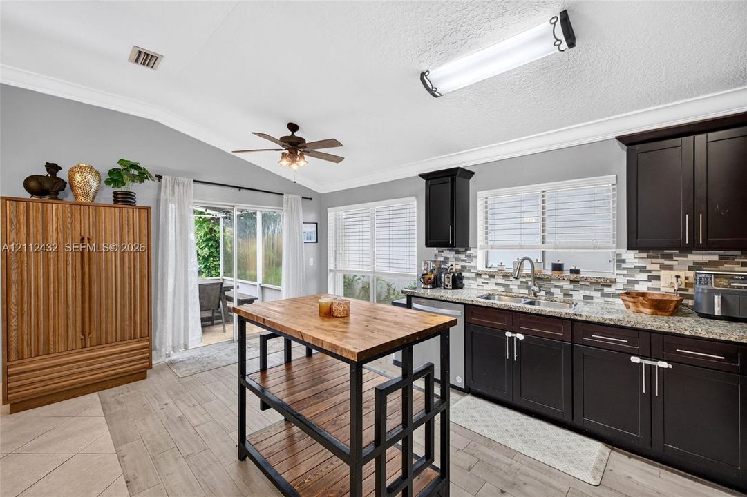Kitchen featuring dark cabinetry, granite-finish countertops, tile backsplash, wood-look tile flooring, and a center island cart with a wood surface