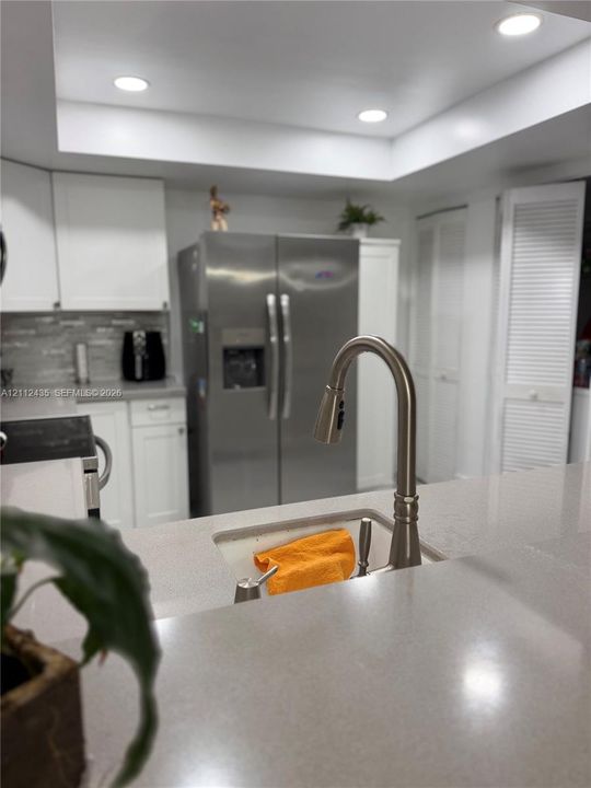 Kitchen featuring quartz countertops, undermount sink with arched pull-down faucet, white cabinetry, stainless steel side-by-side refrigerator, and recessed lighting