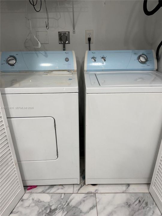 Laundry area featuring a top-loading washer, side-by-side electric dryer, louvered doors, and stone-finish tile flooring