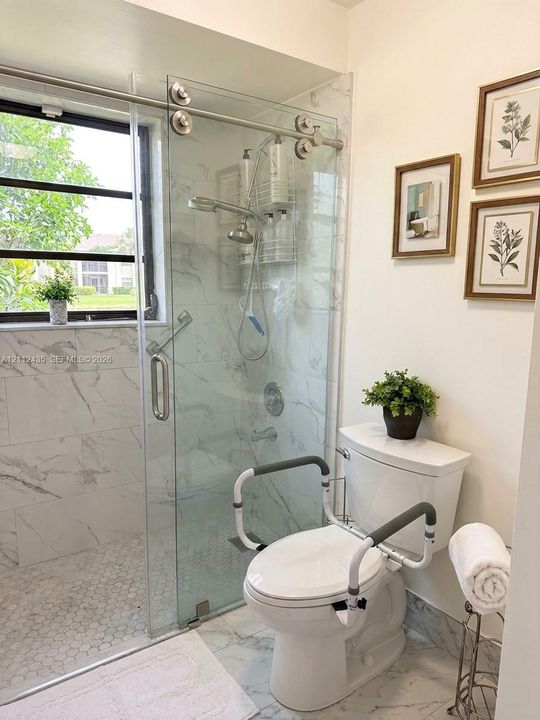 Walk-in shower featuring a sliding glass door, white stone-finish tile surround, hexagon floor tile, and chrome fixtures