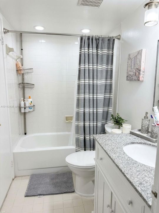 Bathroom featuring a vanity with a light-toned speckled countertop, an integrated sink, white cabinetry, a porcelain tub-and-shower combination with tiled surround, and recessed ceiling lighting