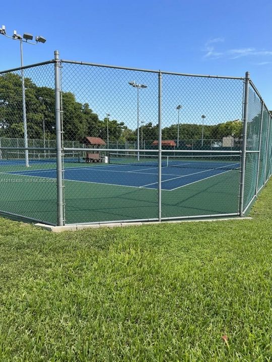 Tennis court featuring a blue and green acrylic surface, chain-link perimeter fencing, and integrated lighting poles