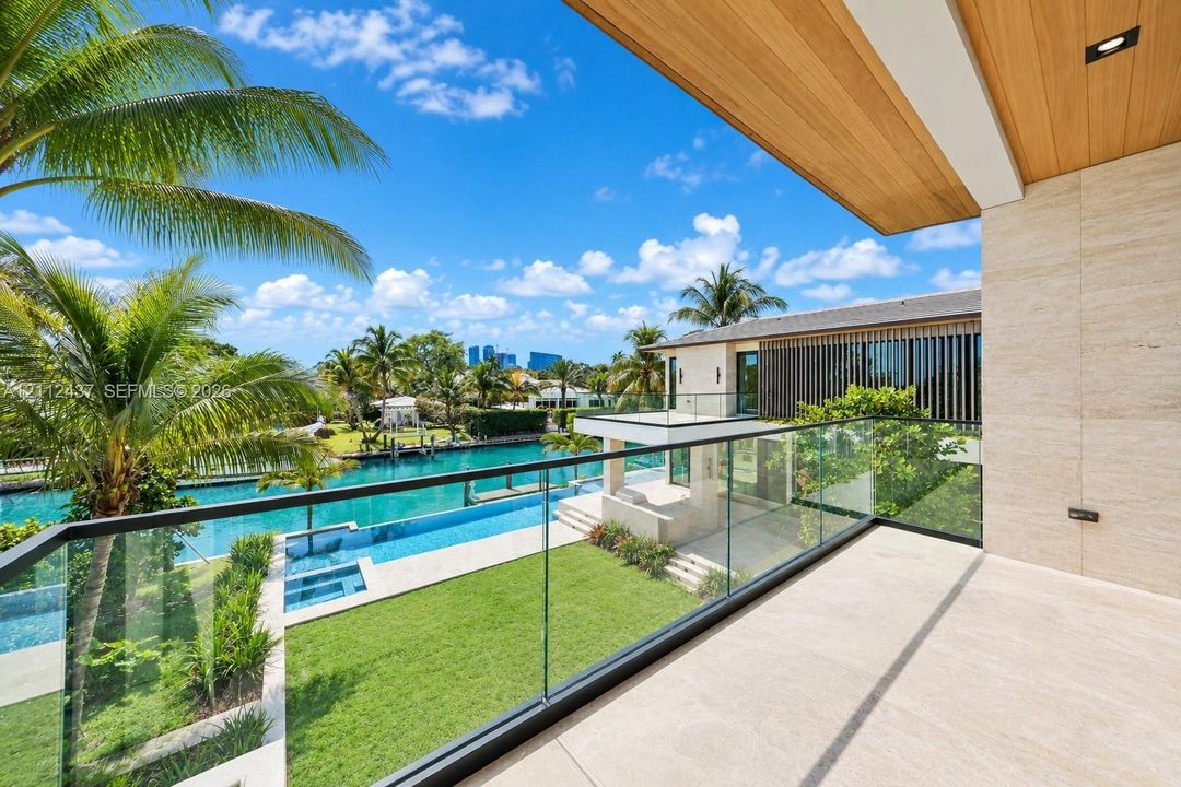Covered balcony featuring stone flooring, wood-plank ceiling, and a frameless glass railing overlooking the waterfront property, swimming pool, and landscaped lawn