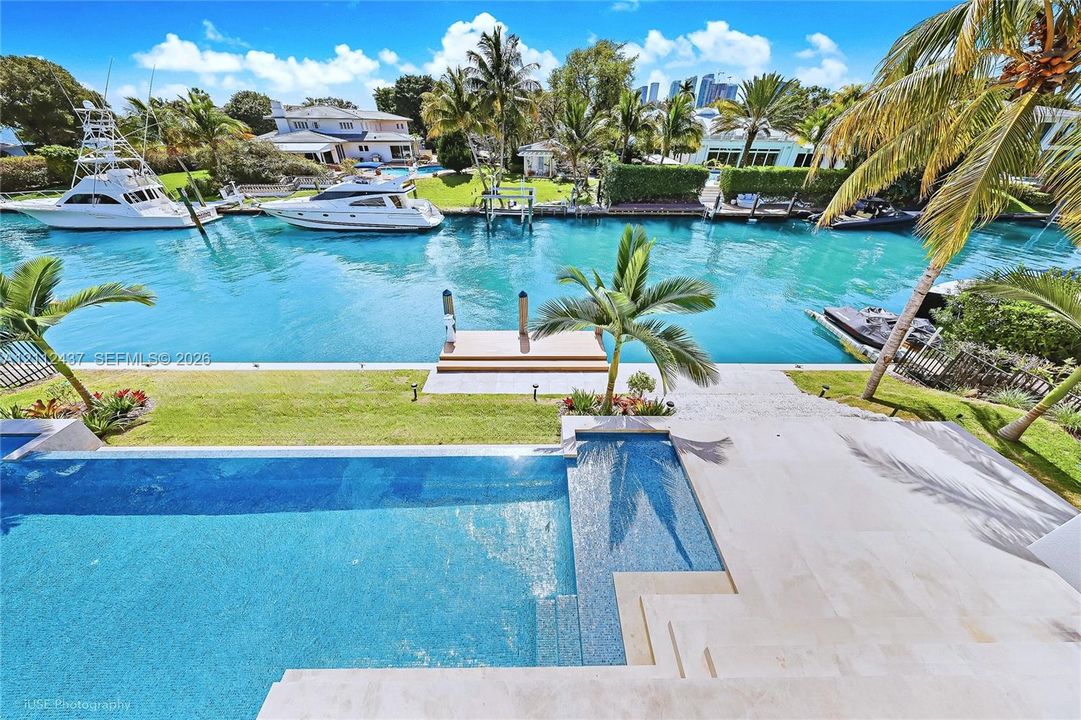 Waterfront estate featuring a paved terrace, swimming pool with integrated sun shelf, private boat dock, and manicured landscaping