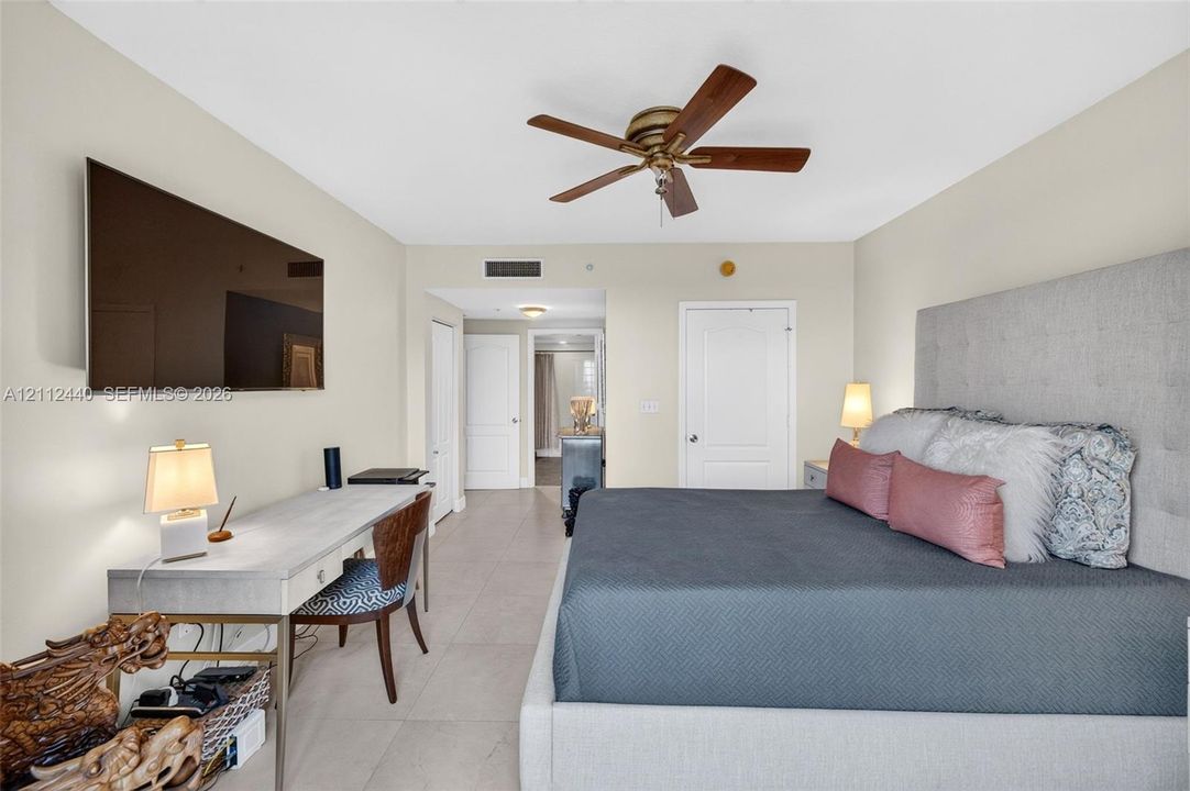 Neutral-toned room featuring large-format porcelain flooring, a five-blade ceiling fan with an integrated light fixture, and two separate closets
