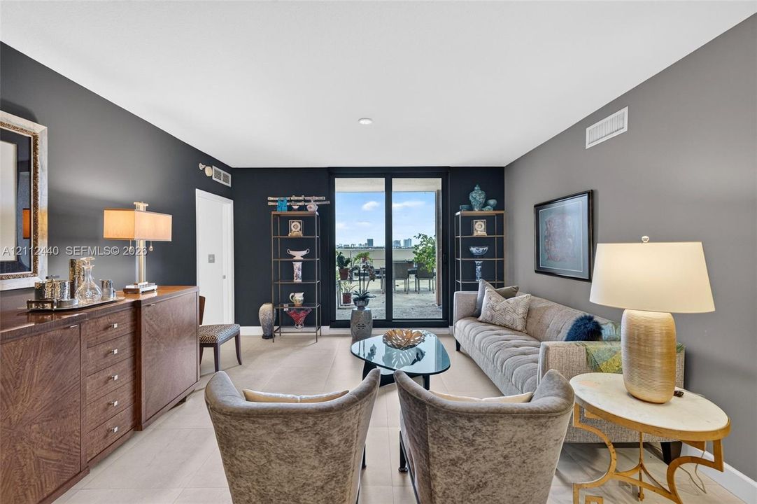 Living area featuring large-format porcelain flooring, high-contrast dark accent walls, and floor-to-ceiling glass sliding doors opening to an oversized outdoor patio