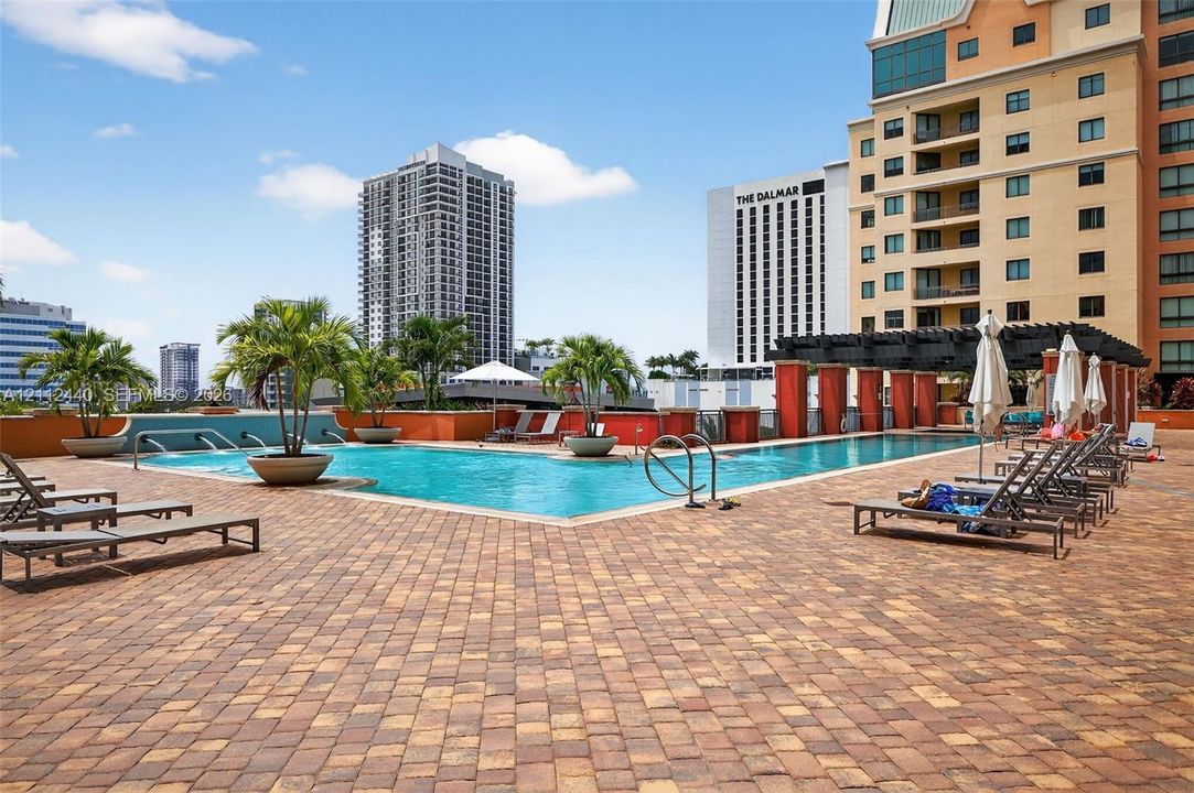 pool deck featuring stone paver flooring, integrated water fountains, a decorative pergola, and tropical planters