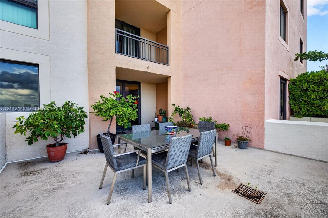 Spacious concrete patio featuring a stucco exterior, a covered balcony with a metal railing, and low-rise wall enclosures