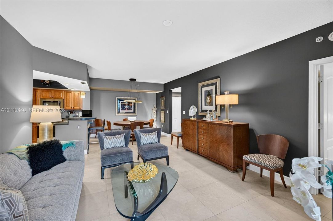 Open-concept interior featuring large-format porcelain flooring, accent wall, and built-in kitchen cabinetry with breakfast bar