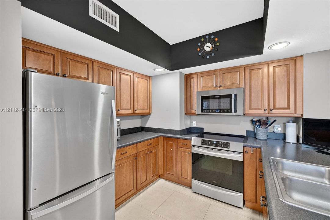 Kitchen featuring upgraded wood cabinets, stainless appliances, dark countertops, recessed lighting, and porcelain flooring