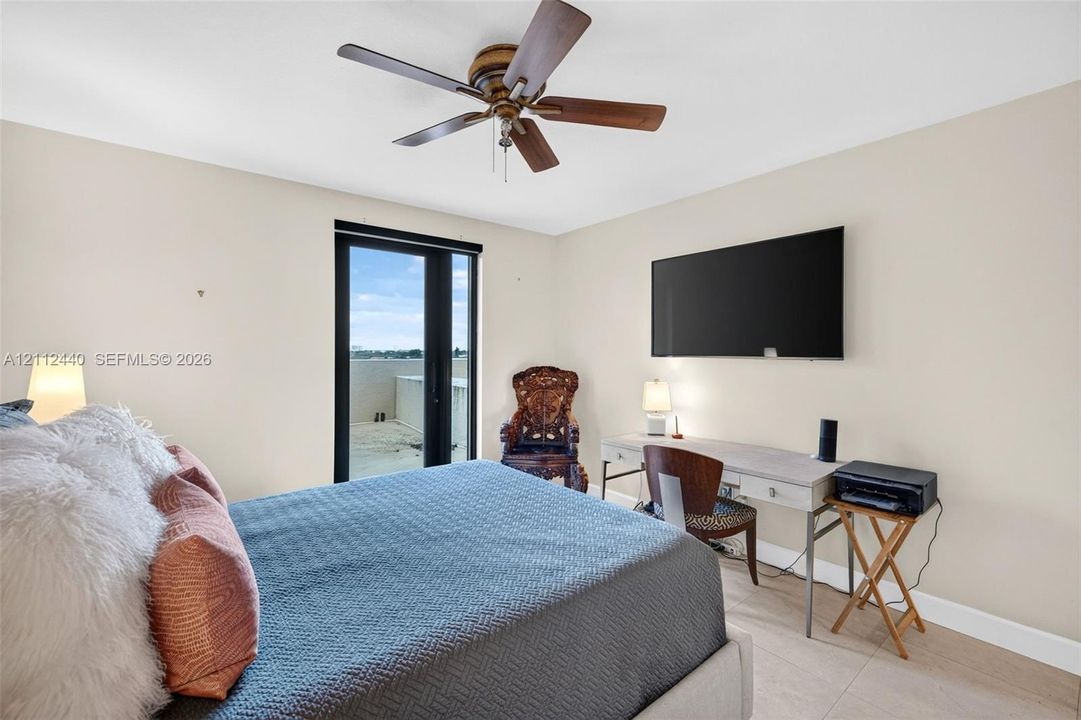 Neutral-toned interior featuring large-format porcelain flooring, a mounted ceiling fan with wood-tone blades, and a sliding glass door providing access to an exterior terrace